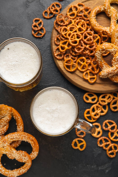 Mugs of fresh beer and pretzels on dark background. Oktoberfest celebration - Fotografie, Obrázek
