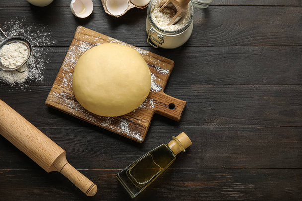 Raw dough with ingredients and utensils on dark wooden background - Zdjęcie, obraz