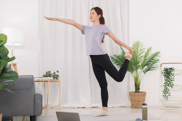 Yoga exercise concept, Young Asian woman stretching leg and arm while doing yoga exercise online. - Fotó, kép