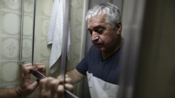 Депрессивный пожилой мужчина, страдающий перед зеркалом в ванной - Кадры, видео