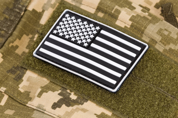 Наклейка винилового флага США в черно-белой цветовой гамме с застежкой-крючком, закрепленной на военной камуфляжной форме, крупным планом в селективном фокусе - Фото, изображение