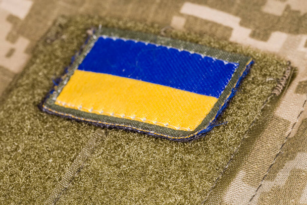 Textile ουκρανική σημαία αυτοκόλλητο με άγκιστρο-και-βρόχο στερέωσης σε στρατιωτική στολή καμουφλάζ, close-up σε επιλεκτική εστίαση - Φωτογραφία, εικόνα