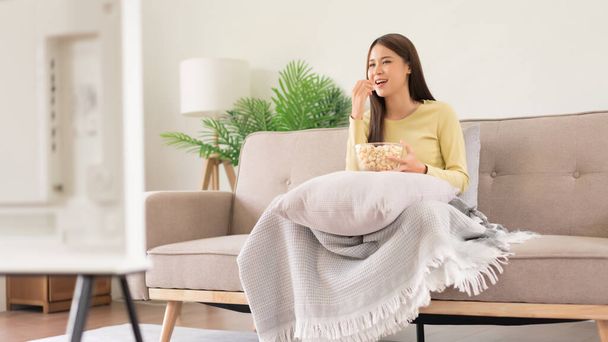 Concept of activity in home, Young woman eating popcorn while watching movie and sitting on couch. - 写真・画像