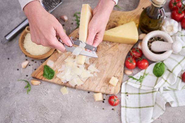Woman slicing Parmesan cheese on a wooden cutting board at domestic kitchen. - Zdjęcie, obraz