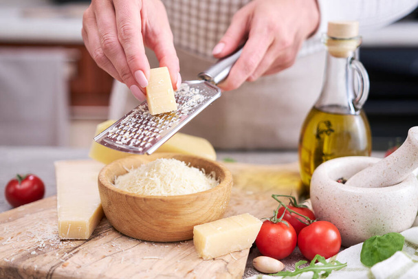 Woman grates Parmesan cheese on a wooden cutting board at domestic kitchen. - Zdjęcie, obraz