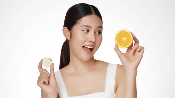 Asian woman are happy with perfect clean healthy skin. Cute female model clean fresh skin is holding sliced of cucumber and orange. Expressive facial expressions. Cosmetology. - Foto, Imagem