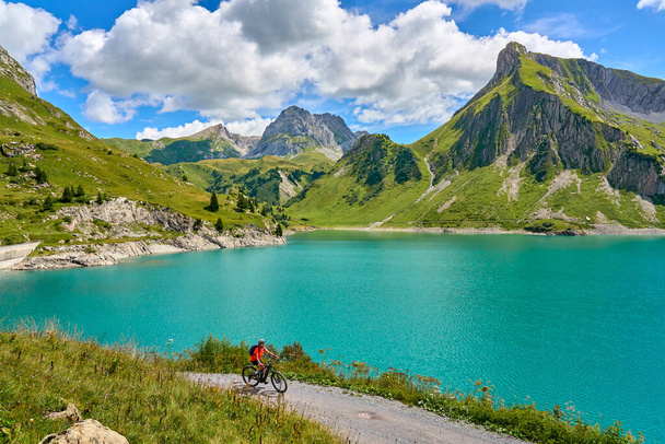 active senior woman, riding her electric mountain bike at Spuller Lake in the Arlberg area near the famous village of Lech, Tirol, Austrian Alps - Foto, imagen