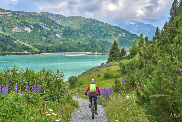 nice active senior woman riding her electric mountain bike in the silvretta mountain range above barrier lake Kopssee,near Gaschurn, Tyrol, Austria - 写真・画像