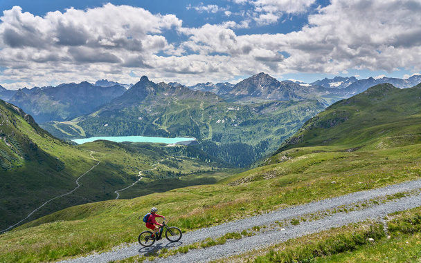 nice active senior woman riding her electric mountain bike in the silvretta mountain range above barrier lake Kopssee,near Gaschurn, Tyrol, Austria - Photo, Image