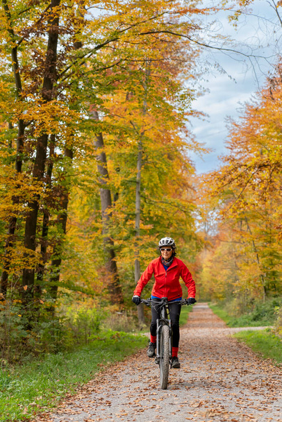 pretty senior woman on electric bicycle in a colorful autumn forest with golden foliage in Baden-Wuerttemberg, Germany - Foto, Imagem