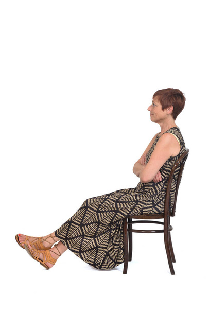 side  view of a middle aged woman sitting on a chair with legs stretched on white background - Foto, Bild