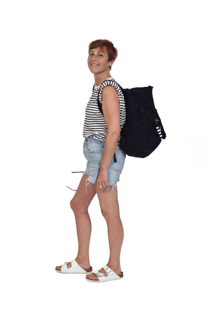 Вид сбоку женщины средних лет в летний день с рюкзаком на камерре на белом фоне - Фото, изображение