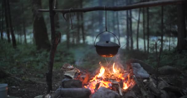 Kettle on a bonfire in the forest. Preparing food on campfire in wild camping. Outdoor recreation concept and Travel in the forest. - Felvétel, videó