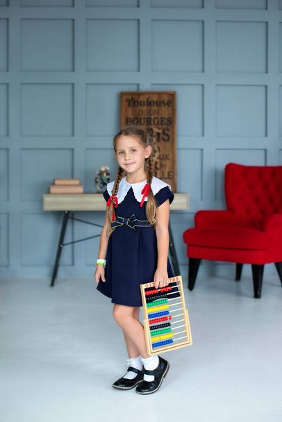 School Girl in school uniform and pigtails hair holds colorful abacus. Back to school, learning lessons. Happy smiling Little girl in dress with abacus. Kid is studying in the classroom in school  - Foto, Imagem
