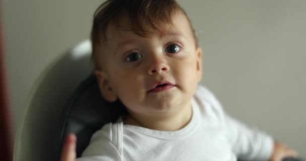 Schattige schattige baby die wijst naar een glimlachende camera. Portret van een kleine jongen zittend op een kinderstoel - Video
