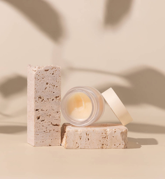 Smass Glass Cosmetic jar on travertine stones on light beige close up, hard shadows. Skincare beauty product package. Exotic natural cosmetics, pastel minimal compositio - Foto, afbeelding