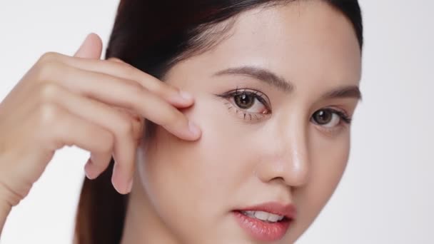 Primer plano retrato de las mujeres asiáticas con cuidado de la cara masajeando suavemente la aplicación de crema hidratante en la mejilla y debajo de los ojos. - Imágenes, Vídeo