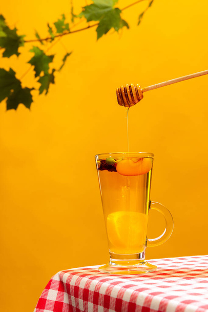 Teacup with delicious sweet tea with citrus, lemons, ginger, honey and mango slice isolated over yellow background. Concept of taste, drink, healthy ingredients, seasonal drink. Copy space for ad - Foto, Imagem