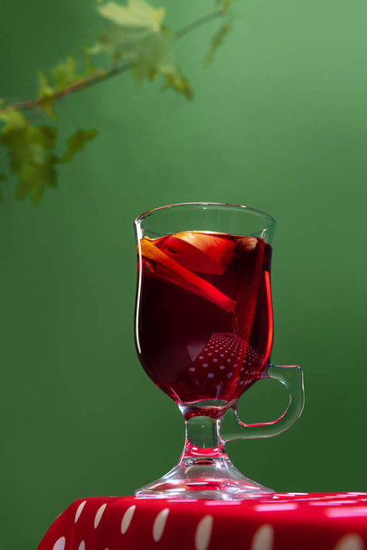 Glass with delicious aromatic cocktail, mulled wine with orange slice and cinnamon stick isolated over green background. Concept of taste, drink, healthy ingredients, seasonal drink. Copy space for ad - Valokuva, kuva