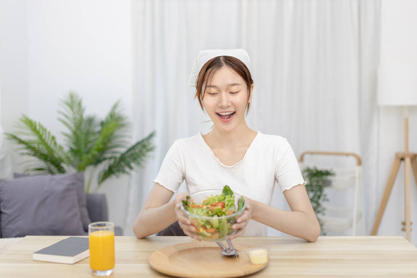 Yemek masasında salata yiyen Asyalı kadın gülümsüyor ve mutlu, sebze salataları vitamin ve mineraller, düşük kalorili ve yüksek lifli diyetler, taze sebze yiyerek sağlık hizmetleri açısından zengindir.. - Fotoğraf, Görsel