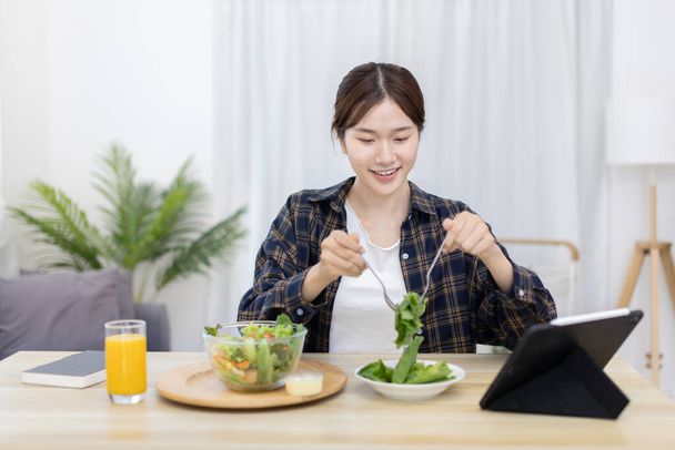 Asian woman eating salad on the dining table smiling and happy, Vegetable salads are rich in vitamins and minerals, Fat-low-calorie and high-fiber diets, Health care by eating fresh vegetables. - Фото, зображення