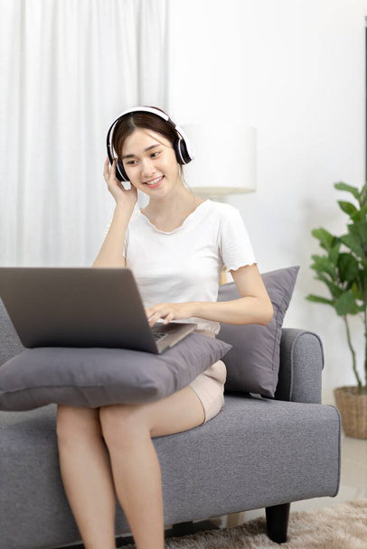 Beautiful Asian woman sits happily listening to music in the living room, Chill, Relaxation time, Happy time, Feel good, Happy weekend getaway, Favorite sofa or Comfort Zone, Feel good. - 写真・画像
