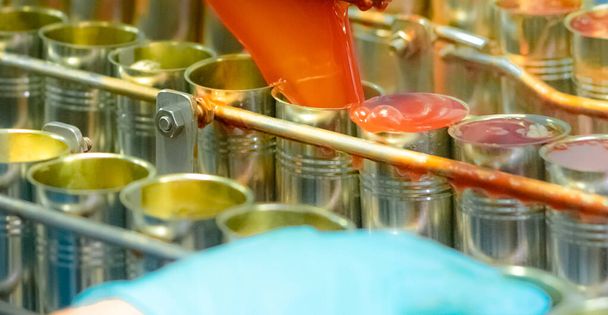 Canned fish factory. Food industry. Machine filling red tomato sauce into sardine can at food factory. Food processing production line. Food manufacturing industry. Cans of sardines on conveyor belt. - 写真・画像