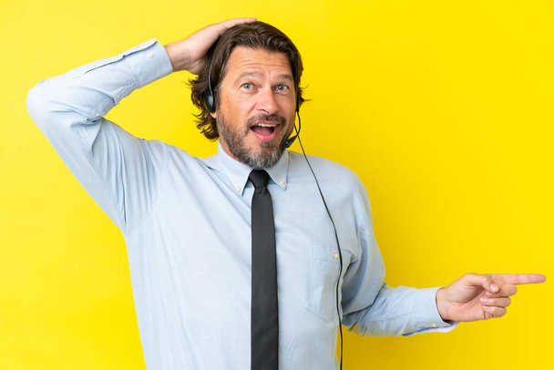 Telemarketer dutch man working with a headset isolated on yellow background surprised and pointing finger to the side - Photo, Image