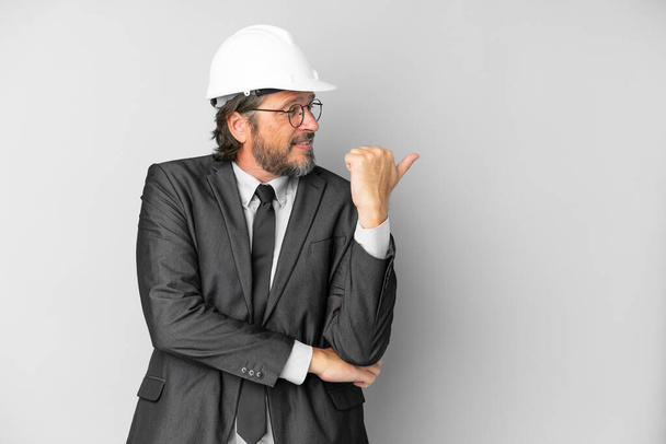 Молодий архітектор чоловік з шоломом над ізольованим тлом, вказуючи на бік, щоб представити продукт
 - Фото, зображення