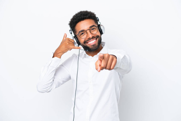 Telemarketer Brazilian man working with a headset isolated on white background making phone gesture and pointing front - Photo, Image
