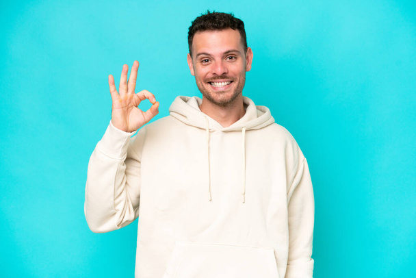 Young caucasian handsome man isolated on blue background showing ok sign with fingers - Foto, Bild