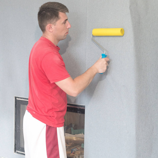a worker glues wallpaper on a wall with a fireplace with the help of a rubber roller, repair work in the house. - Photo, image