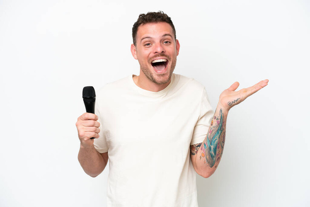 Young caucasian singer man picking up a microphone isolated on white background with shocked facial expression - Fotó, kép