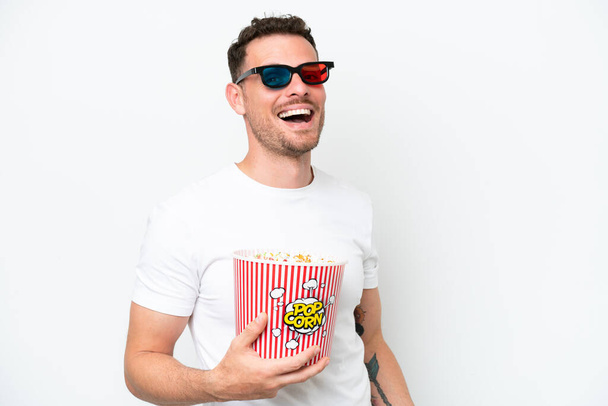 Young caucasian handsome man isolated on white background with 3d glasses and holding a big bucket of popcorns - Photo, Image