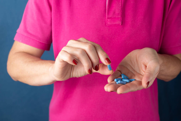 Жінка тримає синю таблетку в руці на синьому фоні. Медичне приладдя
. - Фото, зображення