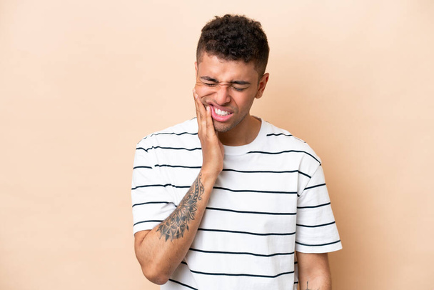 Young Brazilian man isolated on beige background with toothache - Photo, Image