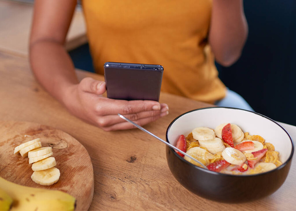 A young woman looks at her cellphone while eating healthy breakfast. High quality photo - Foto, immagini