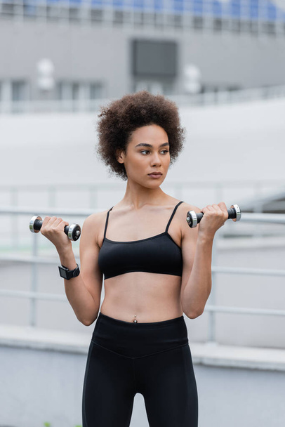 athletic african american woman in black sports bra training with dumbbells - Photo, Image