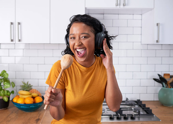 A young funky woman sings with wooden spoon in a modern kitchen. High quality photo - Foto, afbeelding