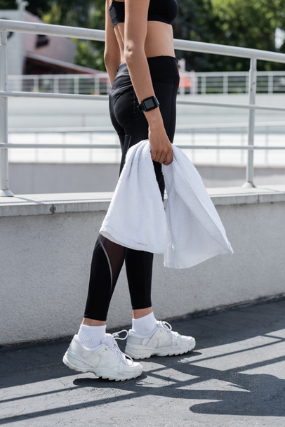 cropped view of african american woman in black leggings and white sneakers holding white terry towel - Foto, immagini