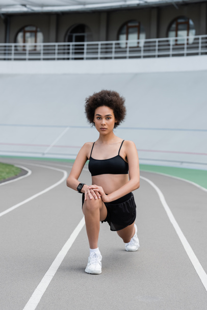 African american sportswoman doing lunges and looking at camera on stadium  - Foto, imagen