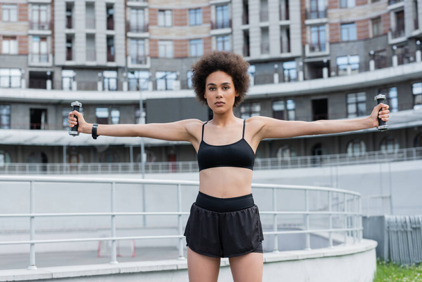 African american sportswoman exercising with dumbbells on stadium at daytime  - Foto, afbeelding