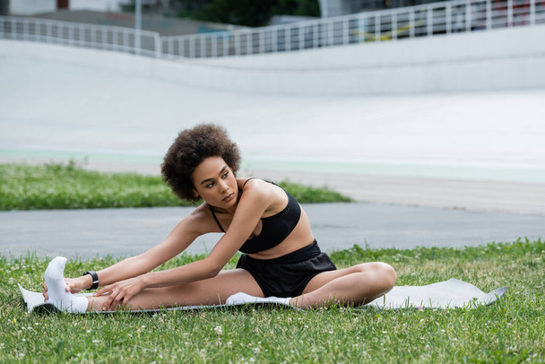 African american sportswoman stretching on fitness mat on stadium  - Foto, Imagem