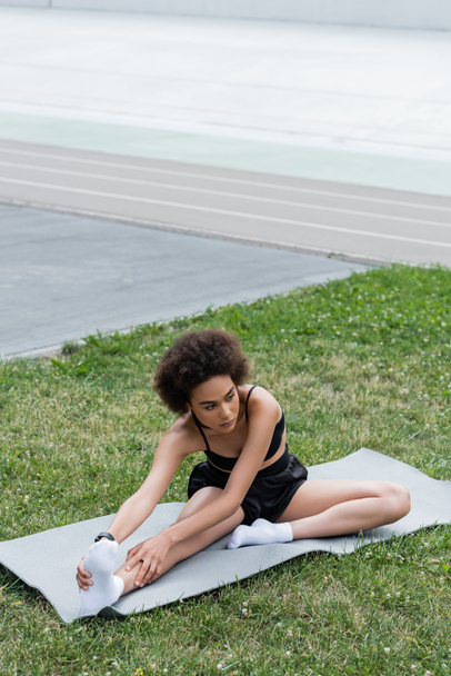 African american sportswoman stretching leg on fitness mat on stadium  - Fotografie, Obrázek