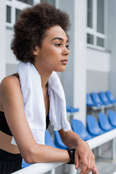 Африканская американская спортсменка с полотенцем, смотрящая на открытый стадион  - Фото, изображение