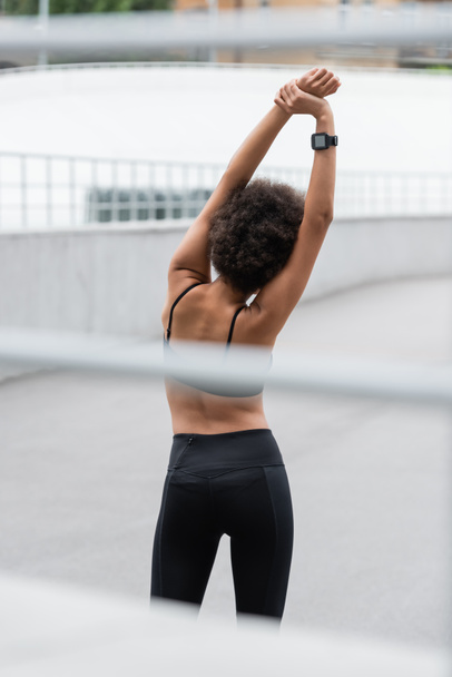 Back view of african american sportswoman with fitness tracker stretching on stadium  - Valokuva, kuva