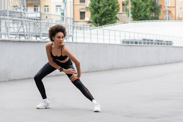 African american sportswoman in top and leggings training on stadium  - Photo, image