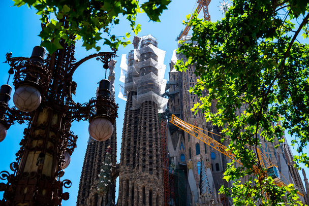 Barcelona, Spain - May 28 2022: In the frame is the famous Sagrada Familia basilica during construction. View through the trees. - Foto, immagini