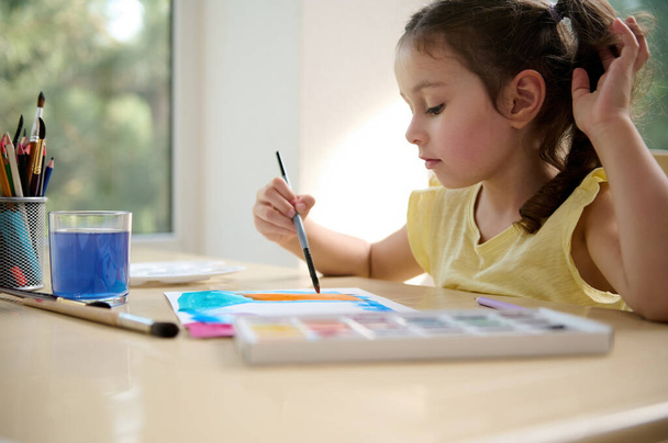 Beautiful cute child, adorable European little girl holding a paintbrush and drawing picture with watercolour paints. Art courses. Painting activity. Kids education and development concept - Zdjęcie, obraz