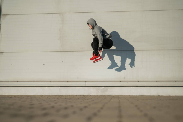 Caucasian man in hoodie jumping high with hands on knees outdoors - Foto, Bild